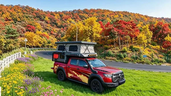 Red pickup with a slide-in camper on a road through autumn hills