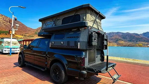 Black pickup with slide-in camper, side door and step open by a lake