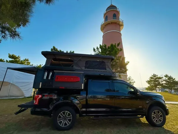 Black Ford F-150 with a slide-in camper beside a lighthouse