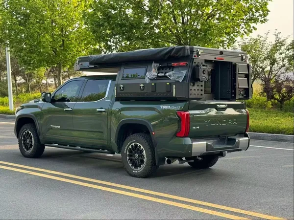 Green Toyota Tundra with a SUNHOMEE slide-in camper on a tree-lined road