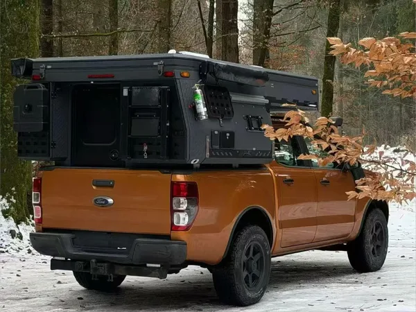 Orange Ford Ranger with a slide-in camper in a snowy forest, rear view
