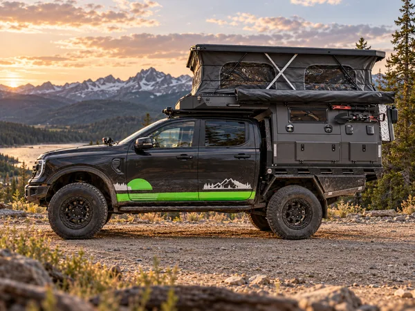 Black Ford Ranger with a SUNHOMEE tray-mount camper, pop-up roof raised, mountain sunset