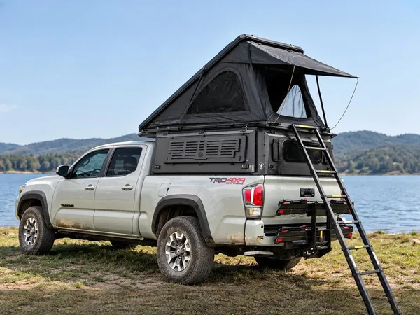 Integrated pop-up topper with the hard-shell tent open on a white Toyota Tacoma by a lake