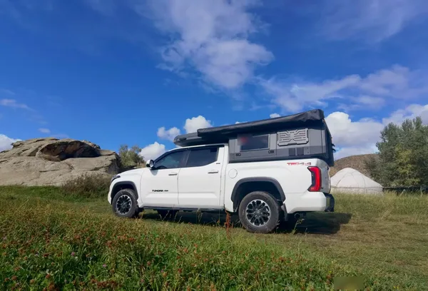 White Toyota Tundra with a SUNHOMEE slide-in camper and awning